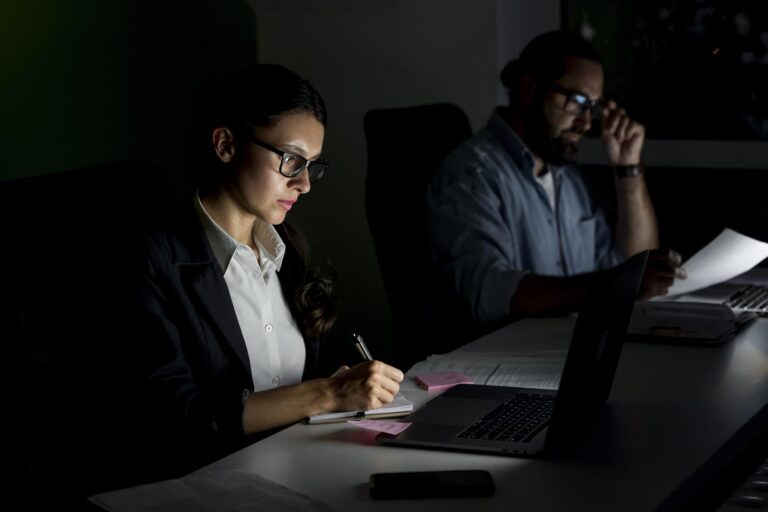 Two colleagues working late at night reviewing financial documents on a laptop